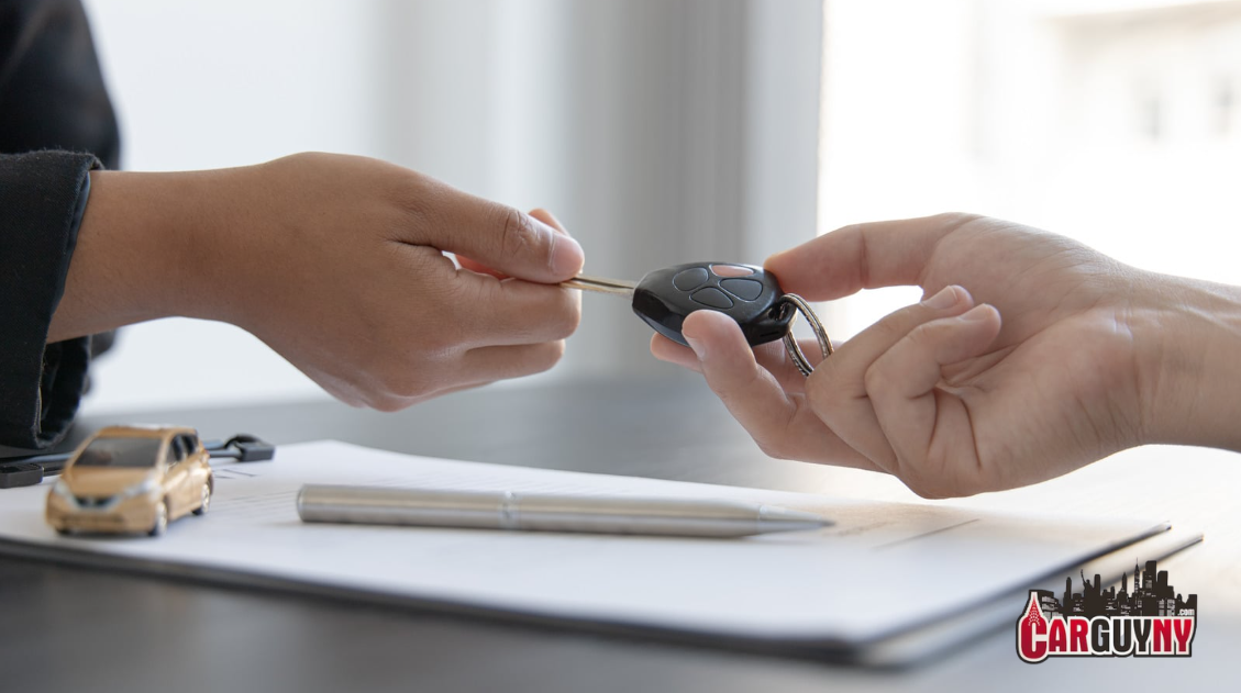 Close-up of two hands exchanging car keys over a document on a table, with a toy car and a pen nearby.